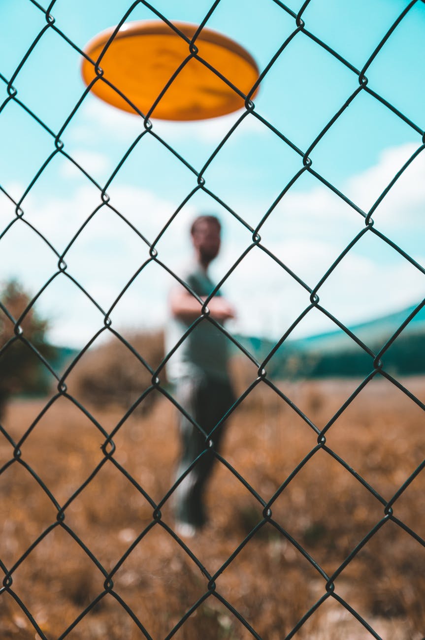 Looking through a chainlink fence to a man throwing a flying disc.