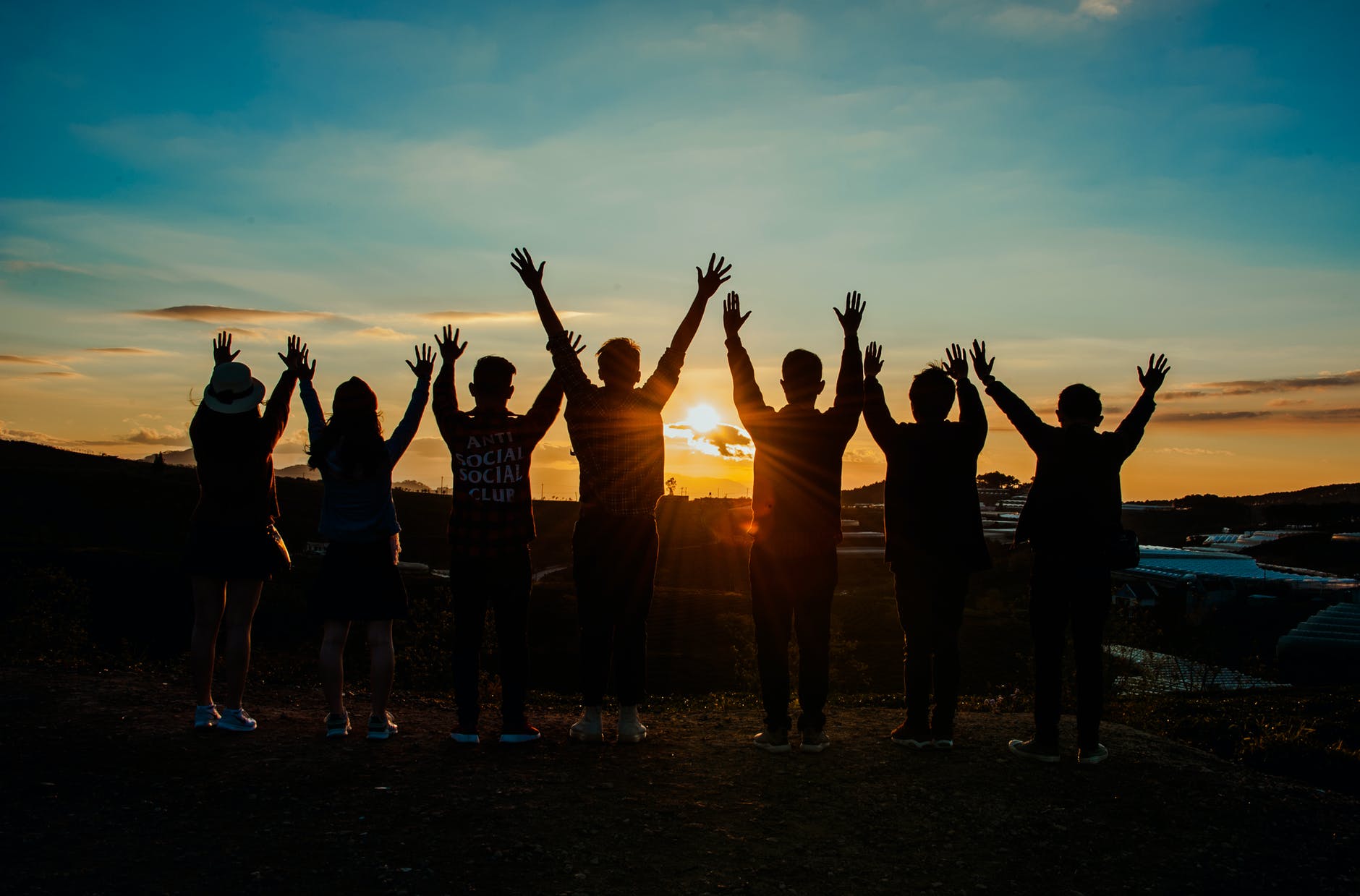 Several people with their arms up looking towards the sunrise.