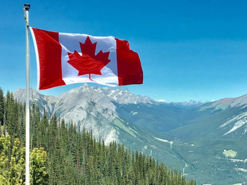 A Canada flag flying in front of some mountains and trees.