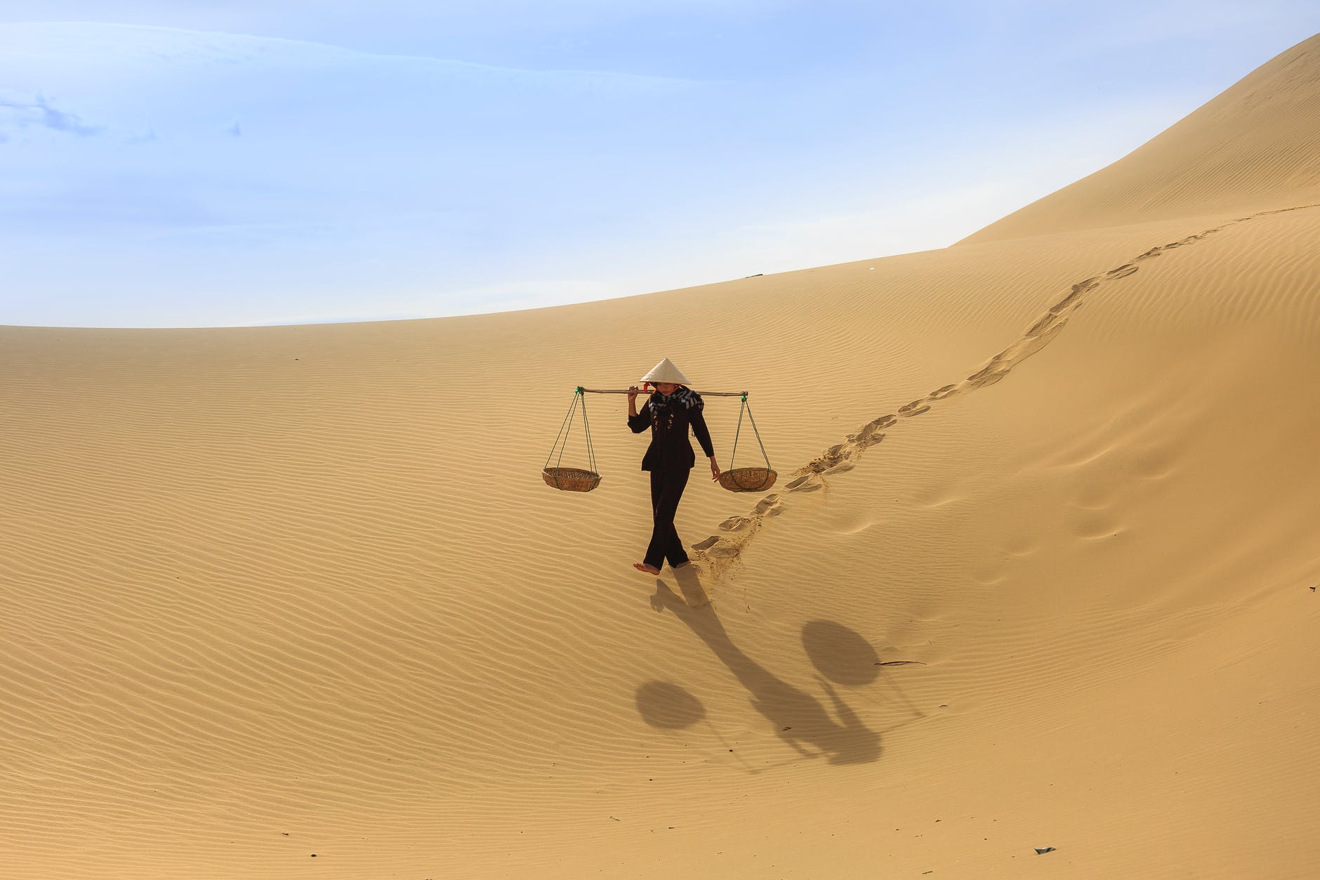 A person with a yoke walking across a sand dune.
