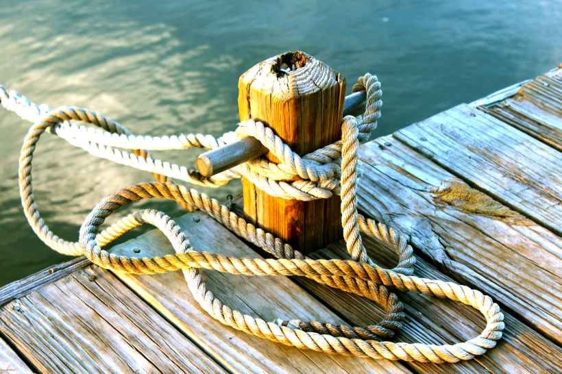 A rope tied to a wooden cleat on a dock.