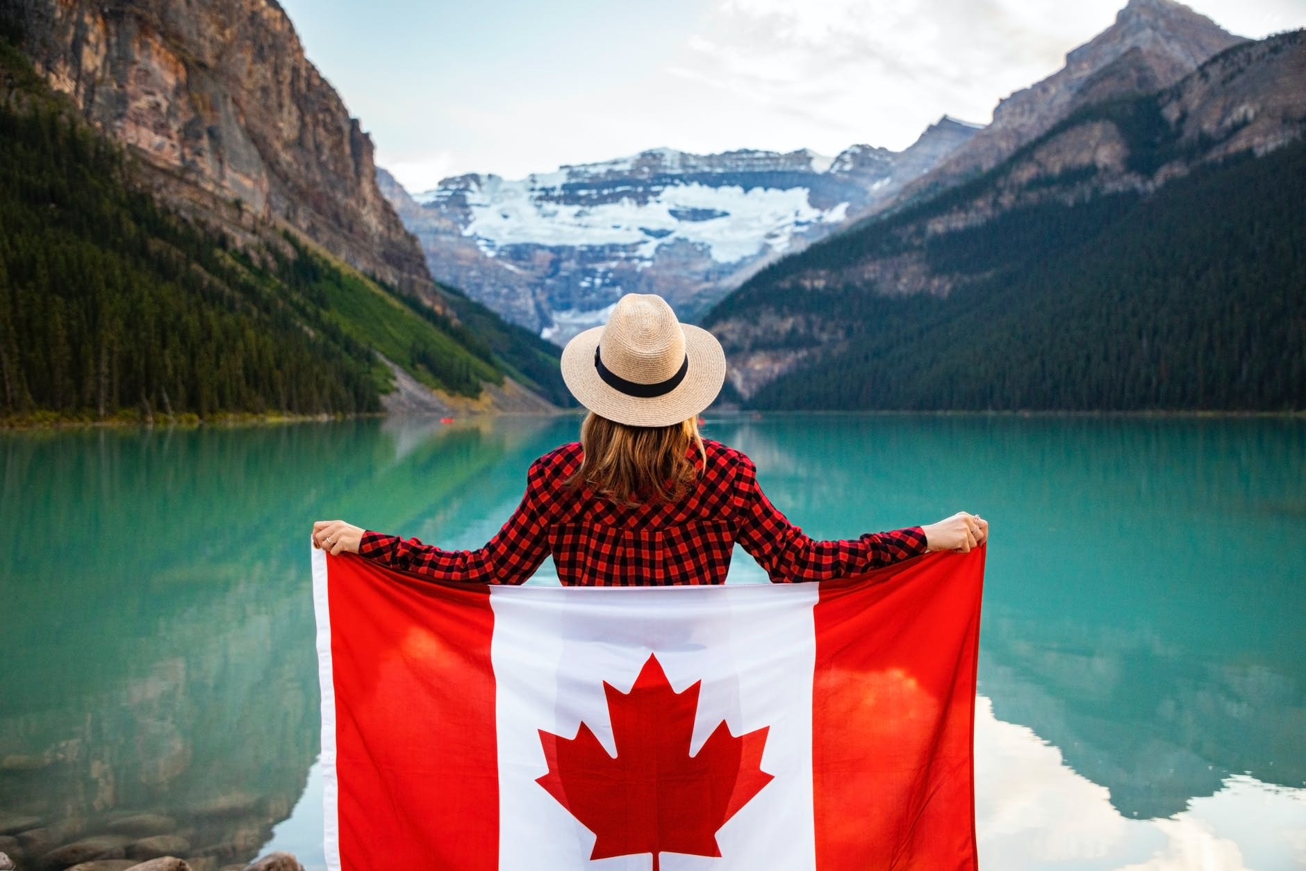 A woman posing with a Canada flag in front of a mountain lake.