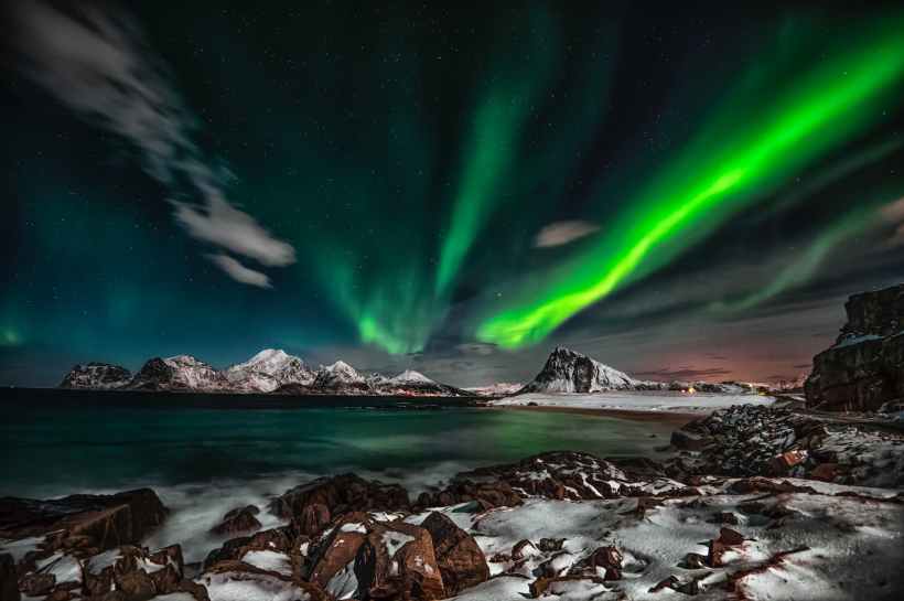 The aurora over a rocky, snowy shoreline.