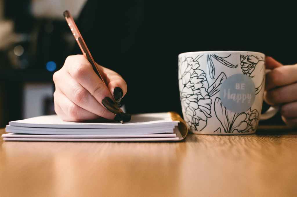 A woman writing while holding a mug.