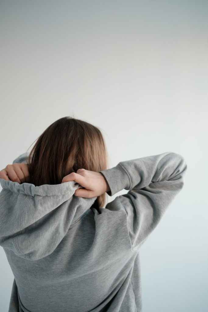 A woman in a hoodie seen from behind holding the hood of her sweater.
