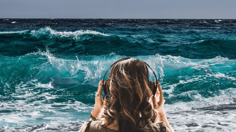 A woman in headphones standing in front of the ocean.