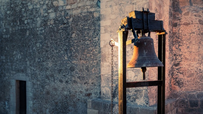 A bell in front of a wall at a church.