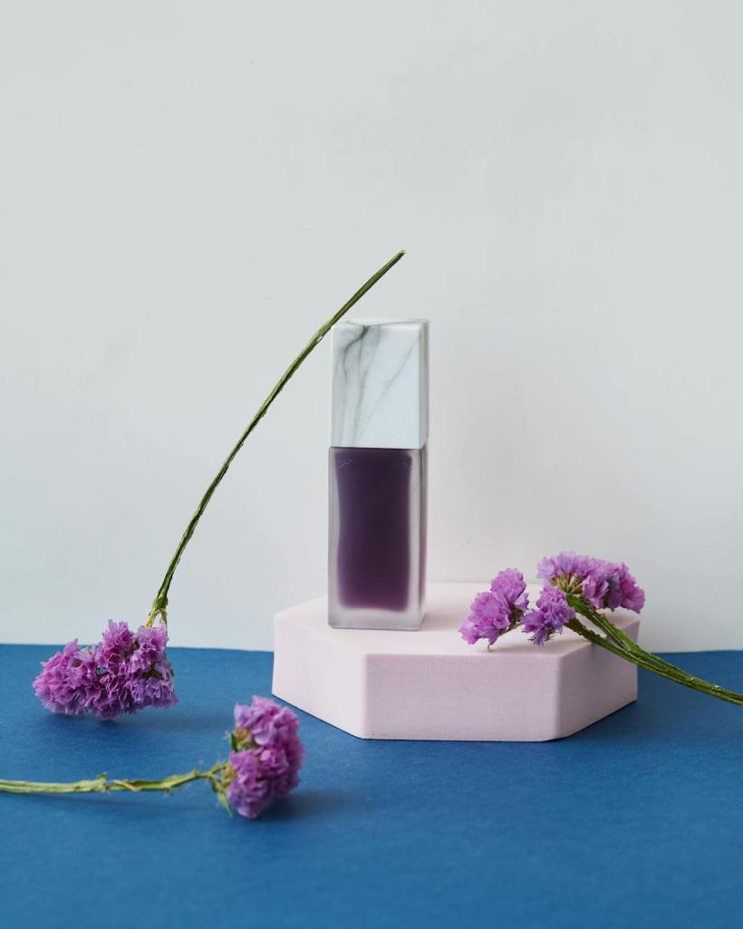A bottle of purple perfume and some flowers.