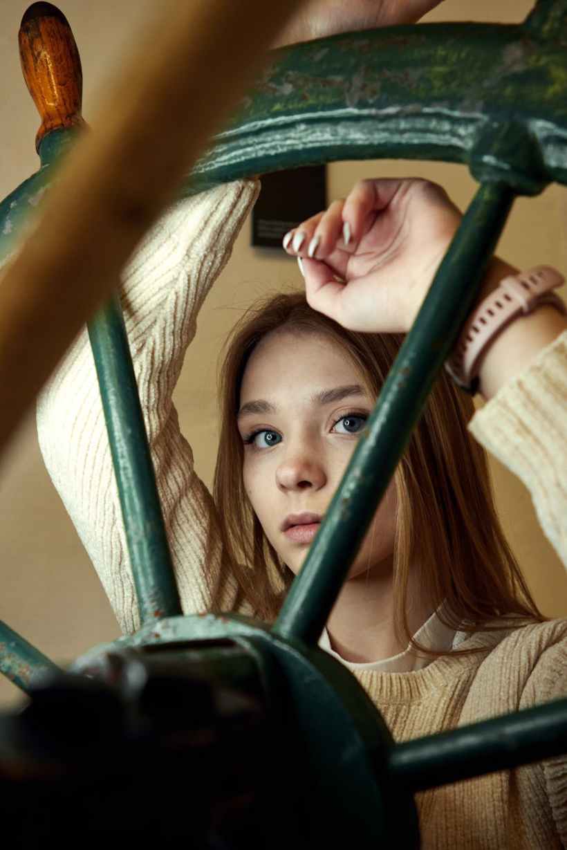 A red-haired girl leaning against a ship's wheel.