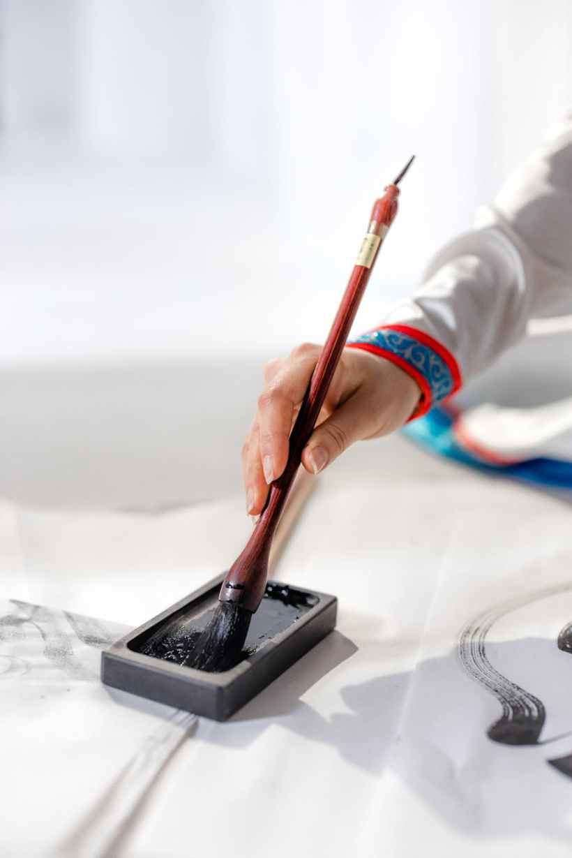 The arm of a person using a traditional East Asian inkbrush.