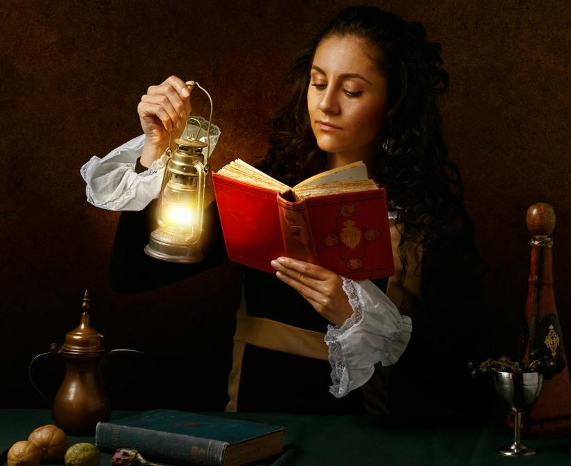 A woman holding a lantern and a book.